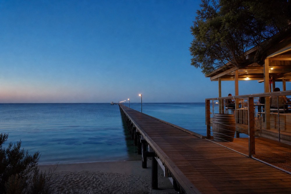 A very long timber jetty reaching straight out over calm turquoise water toward the horizon under a clear sky, no signage, boats or people.