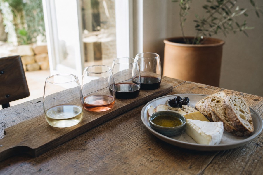 A boutique cellar door tasting flight beside a plate of local produce, olive oil and cheese, soft daylight on a rustic timber table