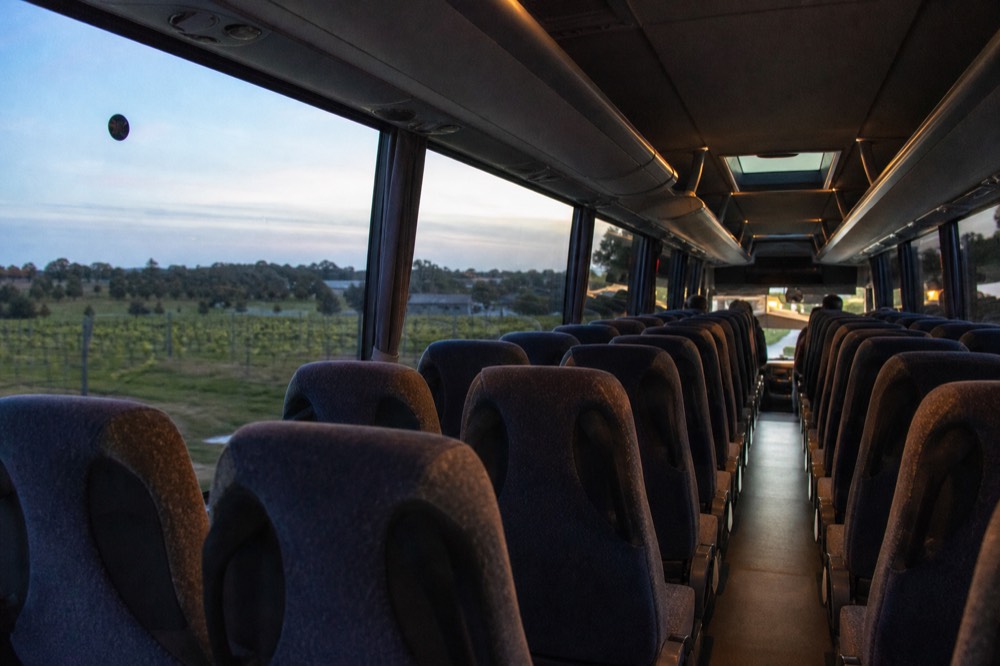 The interior of a comfortable touring coach seen from the aisle, empty upholstered seats and large tinted windows framing green countryside, soft daylight, no logos or passengers.